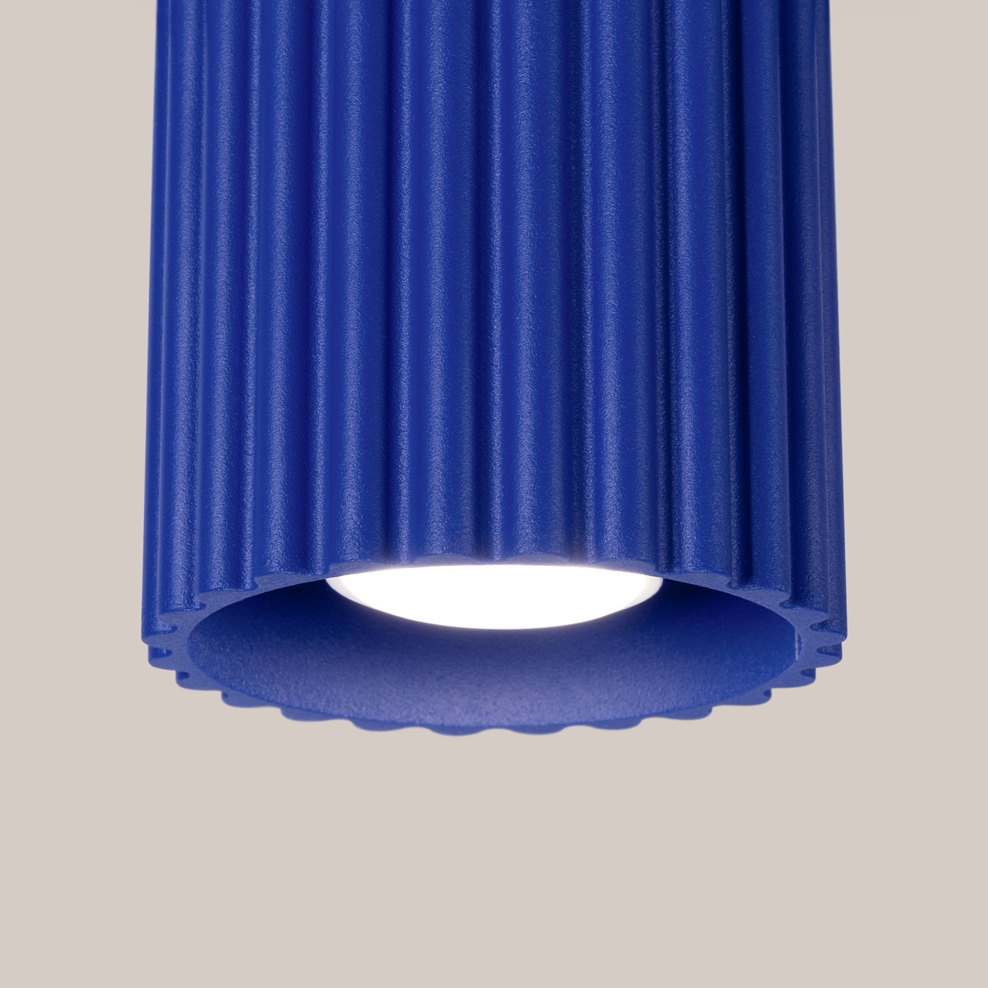 Lampa sufitowa Aura w kolorze ultramaryny, z cylindrycznym kloszem o fakturze z rowkami. Oświetlenie na jedną żarówkę GU10, widok z dołu, ukazujący białą oprawę wewnętrzną. Tło w jasnym odcieniu, co podkreśla intensywność koloru.