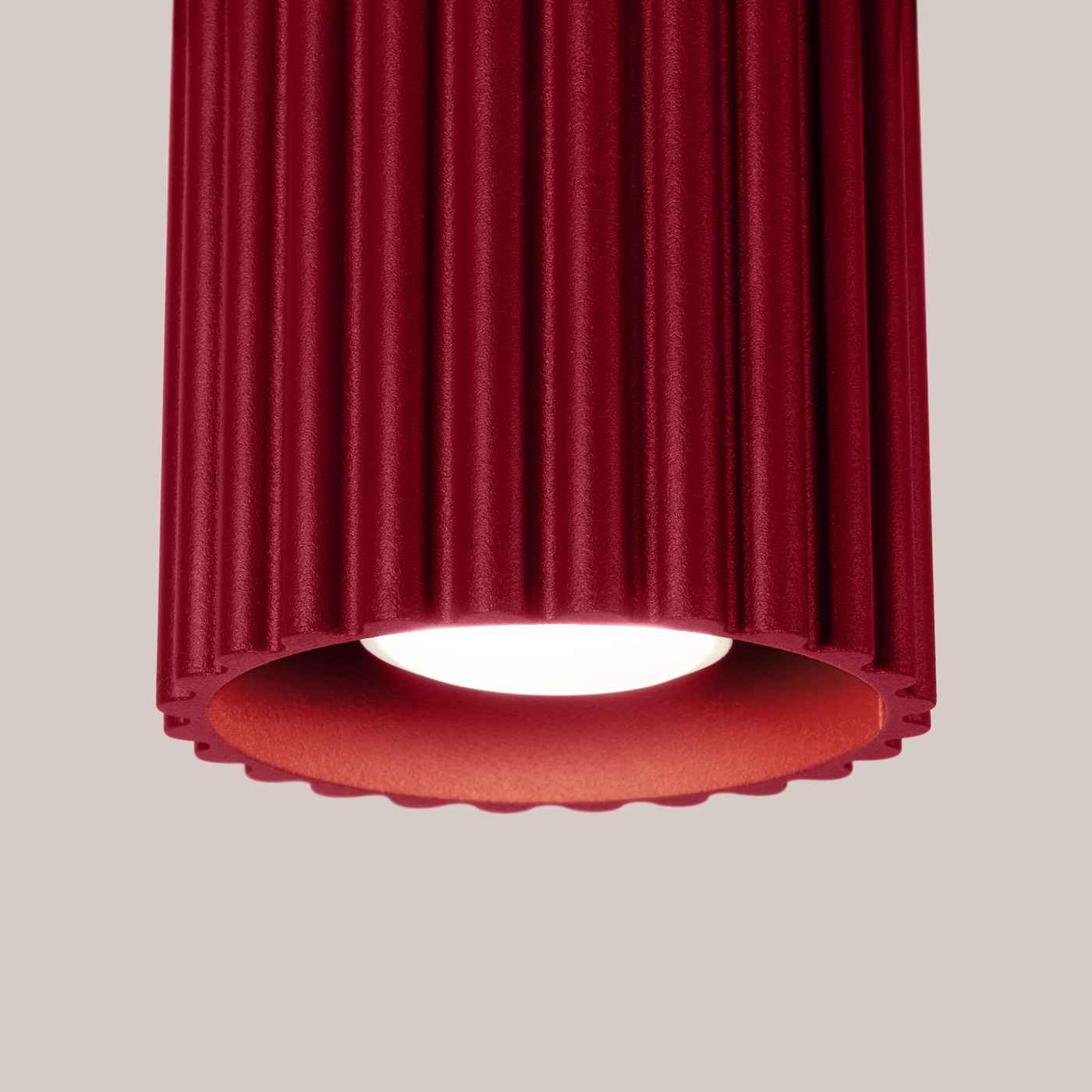 Lampa sufitowa Aura w kolorze burgundowym, z cylindrycznym, teksturowanym kloszem z wyraźnymi żłobieniami. Ujęcie zbliżeniowe na dolną część lampy, odsłaniające źródło światła GU10. Tło w jasnym, neutralnym odcieniu.