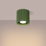 Lampa sufitowa Aura w kolorze oliwkowym, z cylindrycznym kloszem z rowkowanej faktury. Ujęcie z dołu, z widocznym źródłem światła GU10. Tło w pastelowym odcieniu, podkreślające kolor lampy.