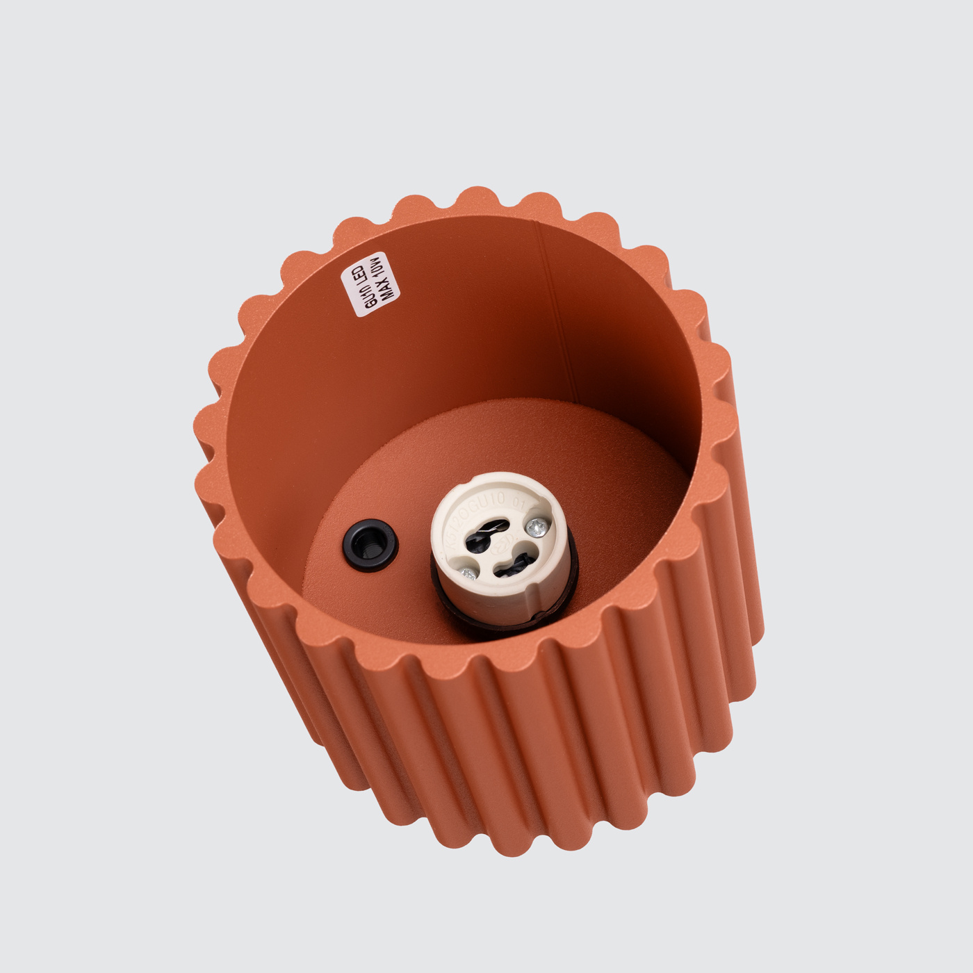 Lampa sufitowa Aura w kolorze ochra czerwona z oprawą o kształcie cylindrycznym, z wyraźnymi, żłobionymi brzegami. Widoczny gwint GU10 oraz otwór do montażu. Wnętrze gładkie, na jasnym tle.