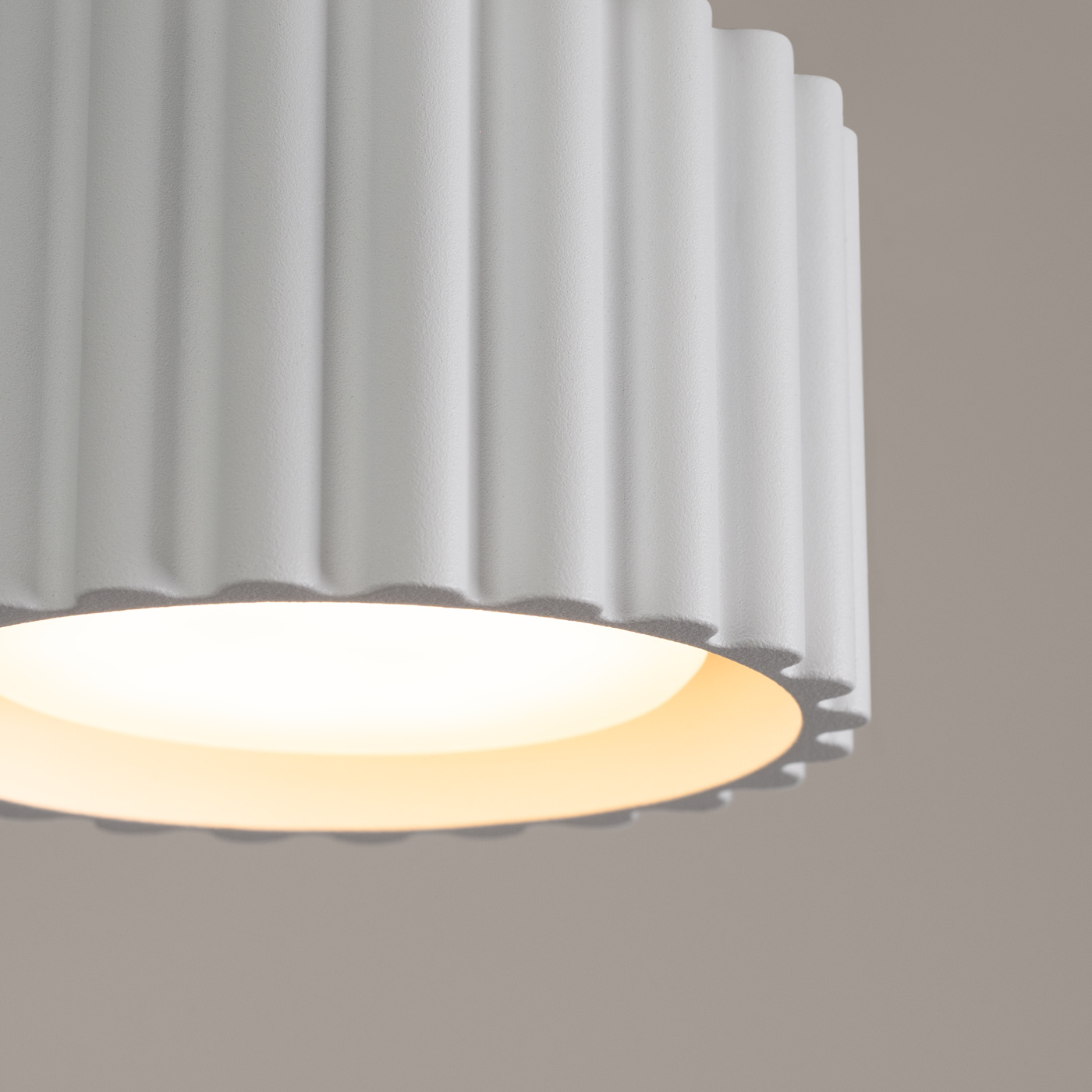 Lampa sufitowa Aura 1xGX53 w kolorze białym, z teksturowanym, falistym kloszem. Ujęcie z bliska na detal klosza, emitującego miękkie światło. Kształt cylindryczny z zaokrąglonymi krawędziami.