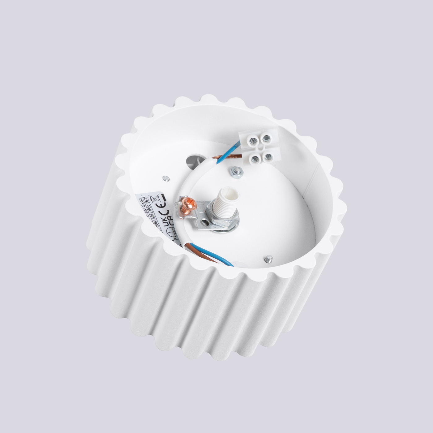 Lampa sufitowa Aura 1xGX53 w kolorze białym, o okrągłej, żłobkowanej obudowie. Widoczna wewnętrzna część z miejscem na żarówkę, przewodami oraz złączami elektrycznymi. Ujęcie z góry, na jednolitym tle.