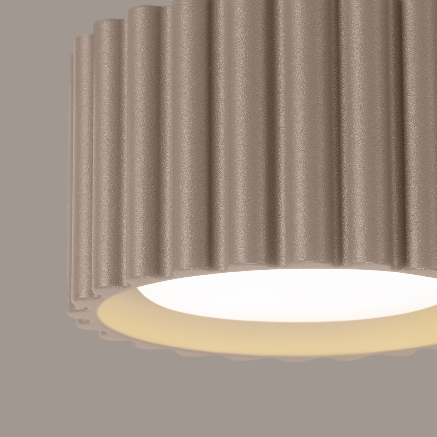 Lampa sufitowa Aura w kolorze taupe z jedną oprawą GX53. Klasyczny, okrągły kształt z fakturowanym, falistym wykończeniem, widoczny biały klosz wewnętrzny. Montowana na suficie, w zbliżeniu na detale struktury.