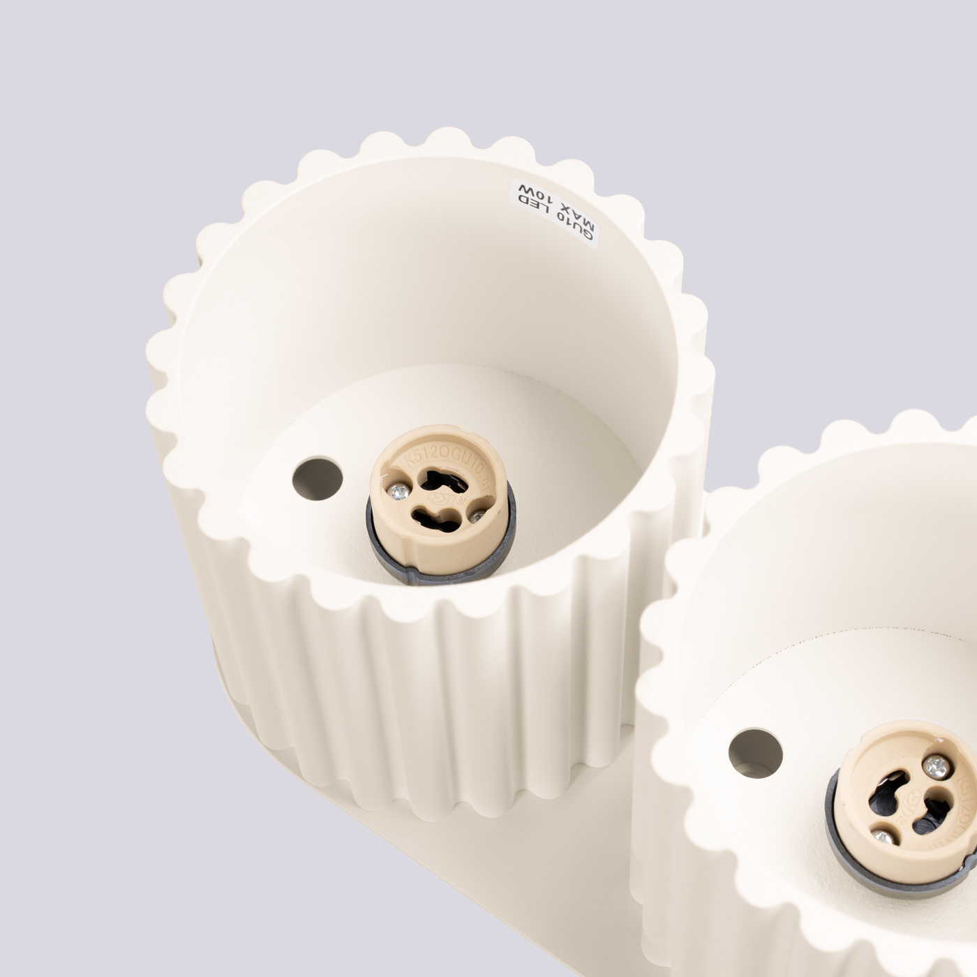 Beżowa lampa sufitowa Aura z dwoma gniazdami GU10, z widocznymi żłobieniami na obudowie. Ujęcie z góry, pokazujące szczegóły gniazd oraz ich kolor. W tle jednolite, jasne.