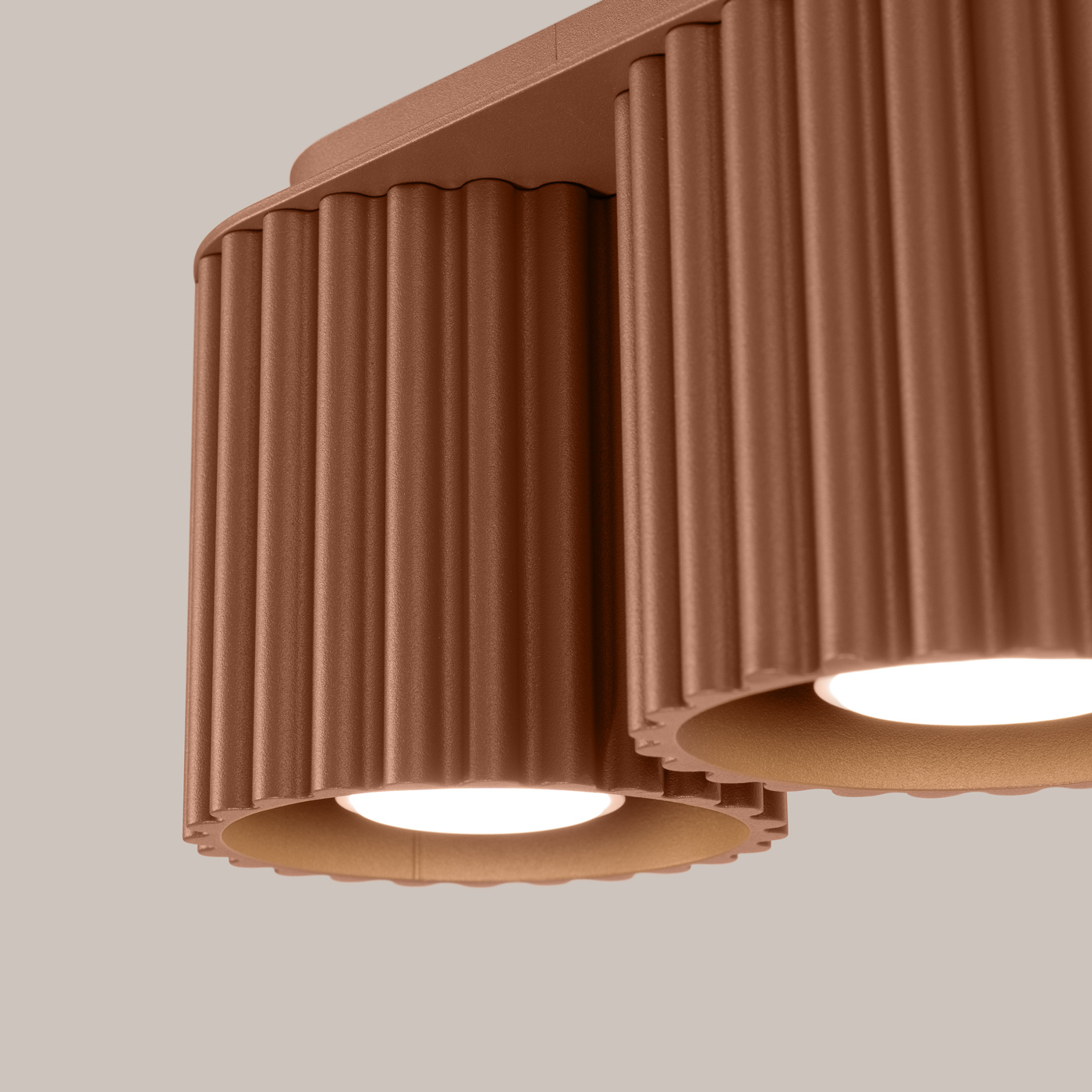 Lampa sufitowa Aura w kolorze mocca z podwójnym źródłem światła GU10. Posiada cylindryczne, żłobione klosze z matowego materiału, zamontowane na prostokątnej podstawie. Ujęcie zbliżeniowe, ukazujące detale i teksturę lampy.