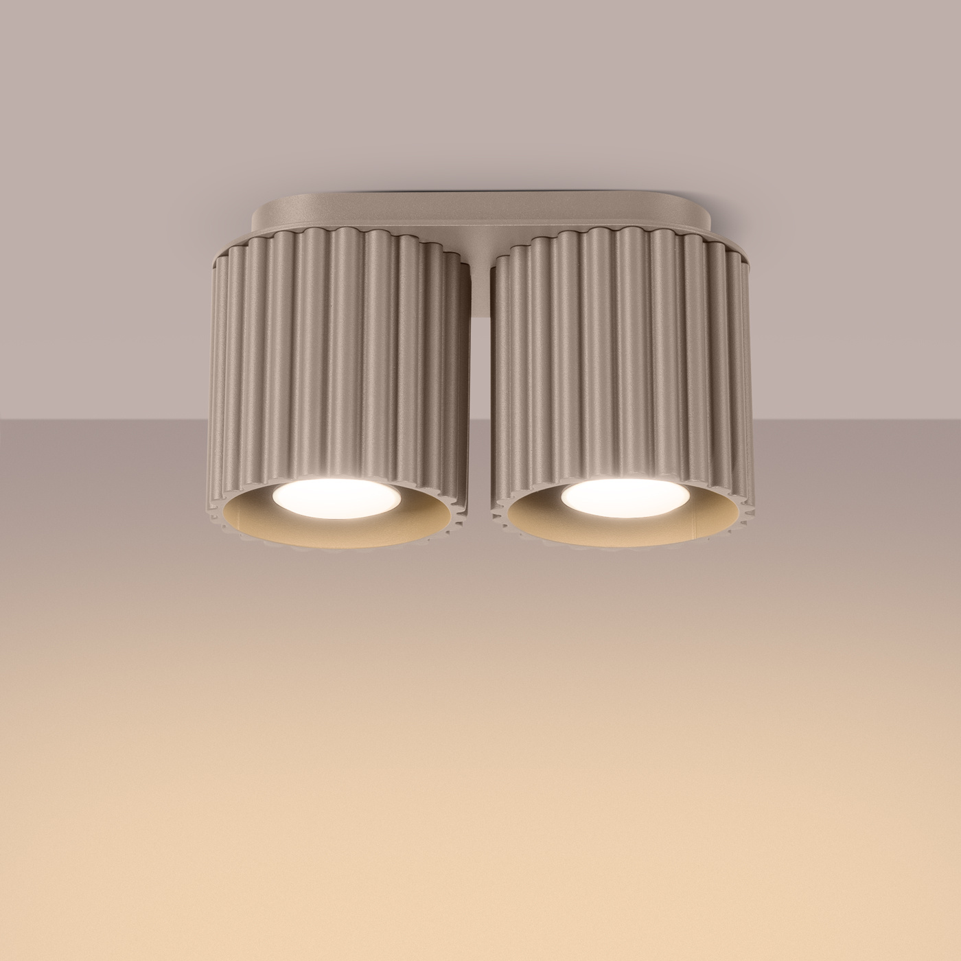 Lampa sufitowa Aura w kolorze taupe z dwoma oprawami GU10. Posiada cylindryczne, żłobkowane klosze, zamontowane na prostokątnej podstawie. Ujęcie z dołu, pokazujące detale kloszy i źródła światła. Tło w odcieniach beżu.