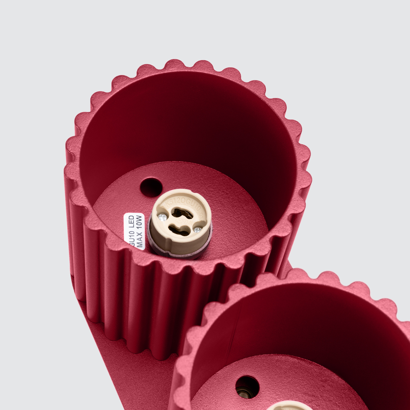 Lampa sufitowa Aura w kolorze burgundowym, z dwoma oprawami na żarówki GU10. Widoczne wykończenie z rowkowanego metalu, z oznaczeniem maksymalnej mocy 10W. Kąt ujęcia z góry, skupiający się na detalach opraw.