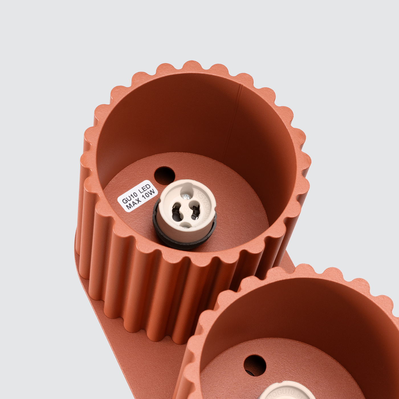 Lampa sufitowa Aura w kolorze ochra czerwona z dwoma gniazdami GU10. Widoczny detal z teksturowanymi, falistymi krawędziami i oznaczeniem maksymalnej mocy 10W dla żarówki LED. Kąt ujęcia z góry, pokazujący wnętrze gniazd.