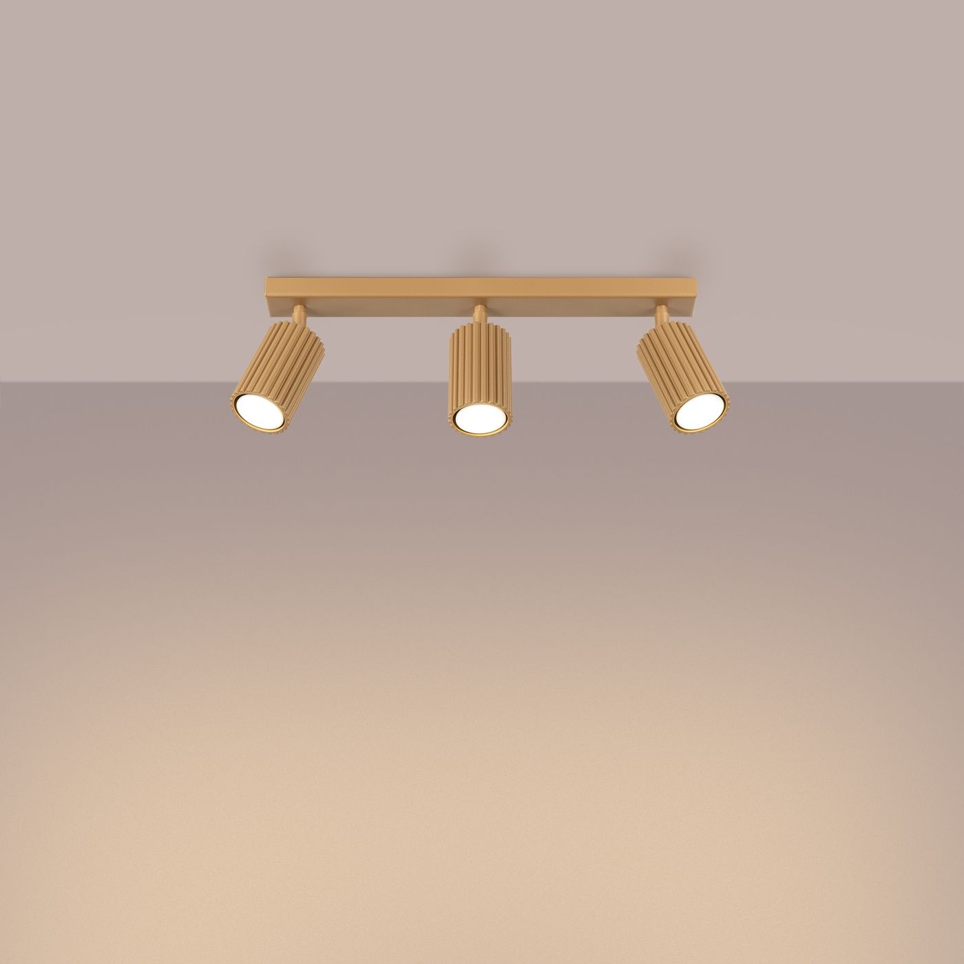 Złota lampa sufitowa Karbon z trzema reflektorami GU10, umieszczona na prostokątnej podstawie. Reflektory mają teksturowaną powierzchnię, skierowane w dół. Tło w neutralnym odcieniu, co podkreśla elegancki design lampy.