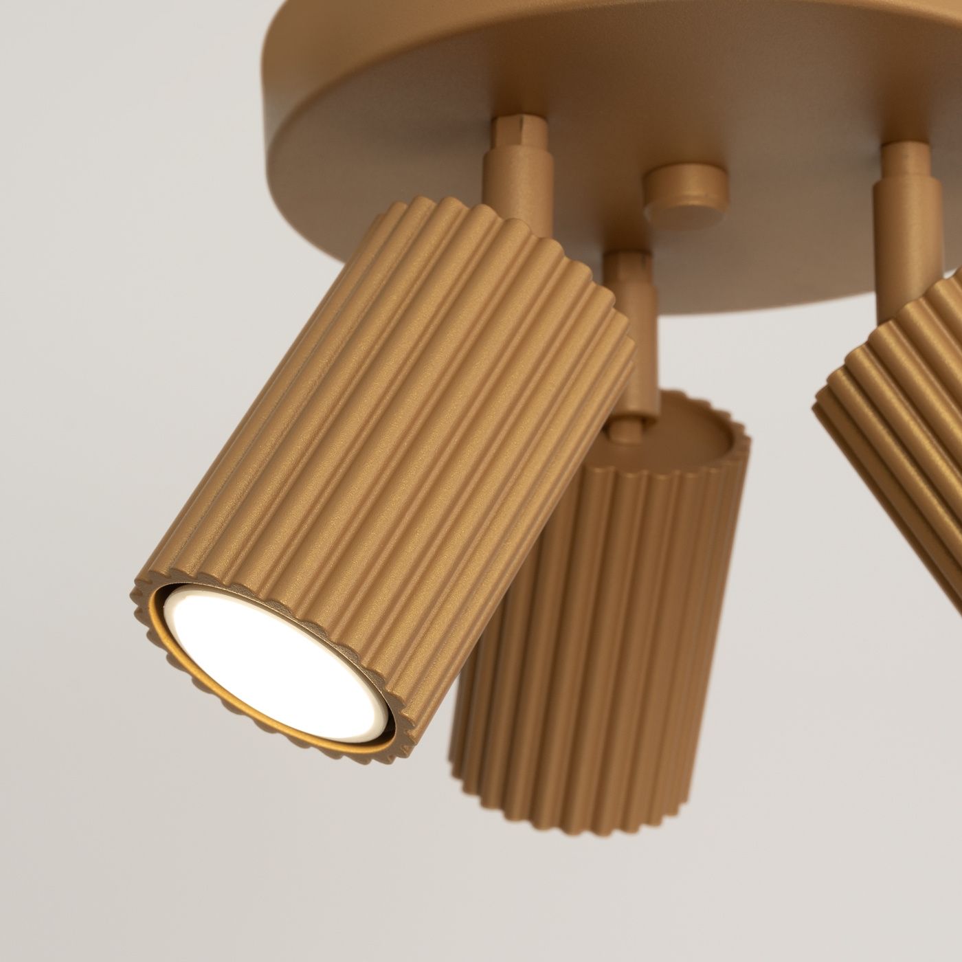 Lampa sufitowa Karbon z trzema reflektorami GU10 w kolorze złotym. Klosze o teksturowanej powierzchni w formie cylindrów, zawieszone na okrągłej podstawie. Widok z bliska na detale struktury i kształtu lampy.