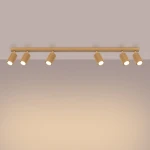Złota lampa sufitowa typu spot z sześcioma regulowanymi oprawkami GU10. Oświetlenie zamontowane na prostokątnej belce, z wyraźnym, teksturowanym wykończeniem w kształcie cylindra. Kąt ujęcia frontalny, na jednolitym tle.