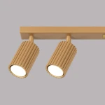 Lampa sufitowa Karbon w kolorze złotym z sześcioma reflektorami GU10. Widoczne dwa cylindryczne lampy z teksturowaną powierzchnią, zamontowane na prostokątnej podstawie. Ujęcie z przodu, na jednolitym tle.