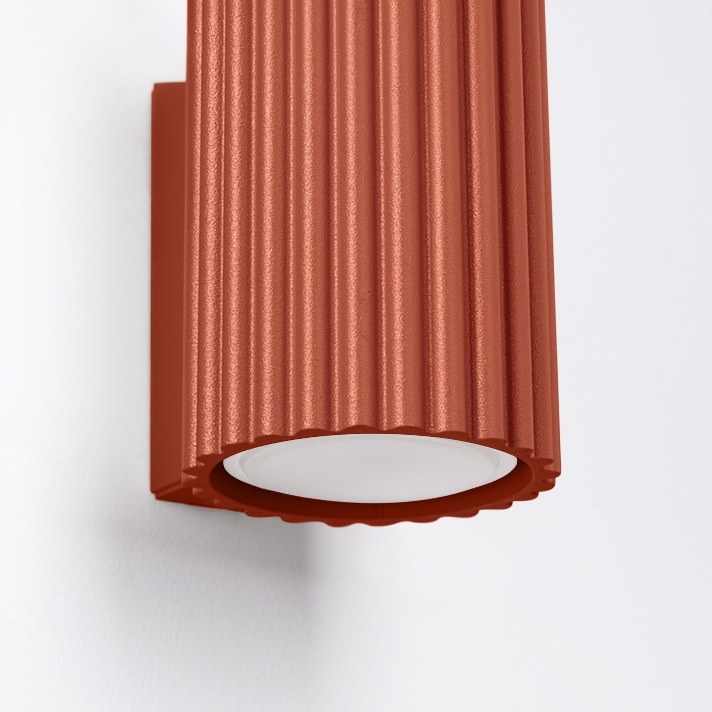 Kinkiet Karbon 10 w kolorze ochra czerwona z żłobioną obudową. Posiada miejsce na jedną żarówkę GU10. Zainstalowany na ścianie, z białą, okrągłą osłoną na dole. Idealny do nowoczesnych wnętrz.