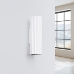 Kinkiet Karbon 20 w kolorze białym, z dwoma gniazdami GU10. Ma cylindryczny kształt z wypukłą fakturą w formie pionowych rowków. Zainstalowany na ścianie w minimalistycznym wnętrzu, na tle dużego okna.