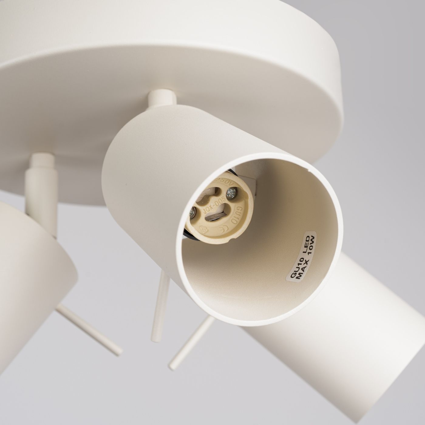 Beżowa lampa sufitowa spot z trzema oprawami GU10, o okrągłej podstawie. Widoczne gniazda na żarówki, metalowa konstrukcja z delikatnym wykończeniem. Kąt ujęcia zbliżony na detale oprawy.