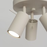 Beżowa lampa sufitowa typu spot z trzema ruchomymi reflektorami GU10. Reflektory cylindryczne, matowe, zamontowane na okrągłej podstawie. Widać jeden włączony reflektor, emitujący jasne światło. Tło jasnoszare, minimalistyczne.