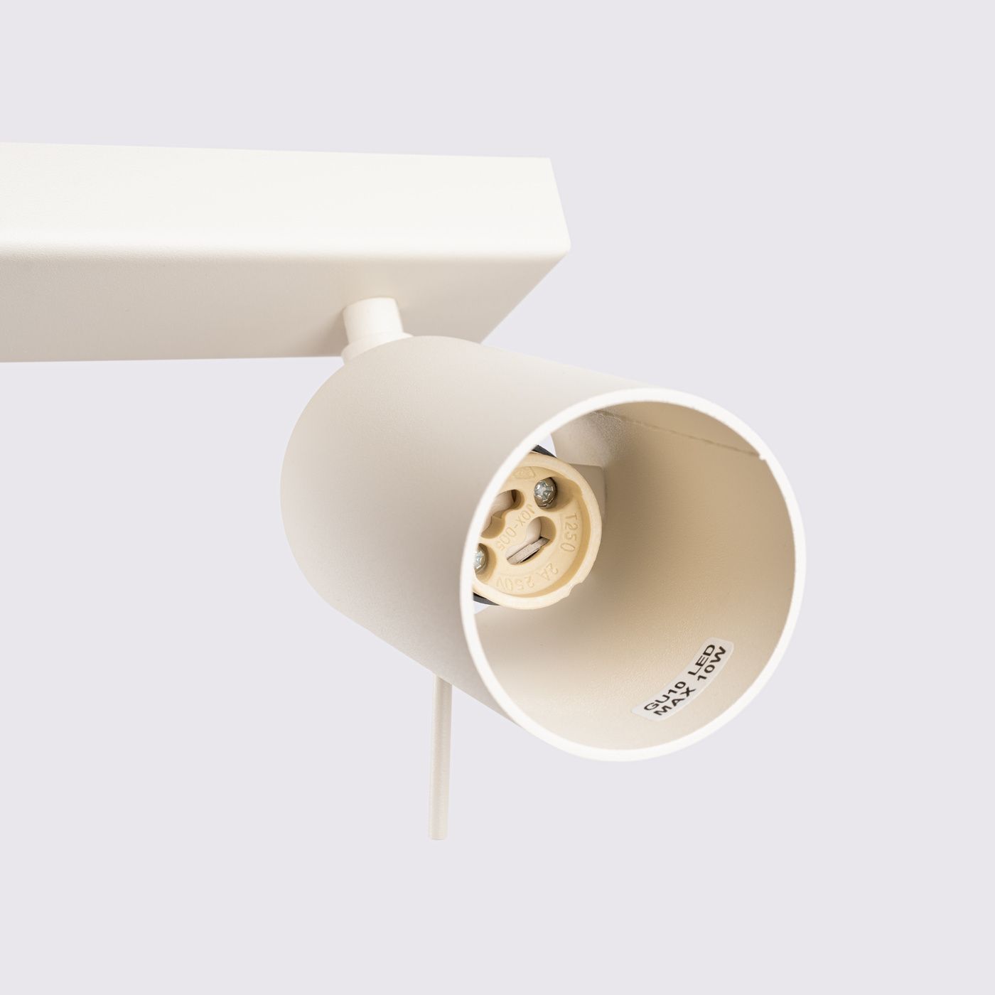 Beżowa lampa sufitowa typu spot z czterema oprawami GU10, zamontowana na prostokątnej podstawie. Widoczny detal oprawy z gniazdem i oznaczeniem maksymalnej mocy 10W. Ujęcie z boku, podkreślające kształt i kolor lampy.