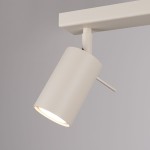 Beżowa lampa sufitowa typu spot z jednym ruchomym reflektorem na wysięgniku, wykonana z metalu. Reflektor ma cylindryczny kształt i emituję światło w dół. Prosta, nowoczesna konstrukcja, montowana na suficie, na jednolitym tle.