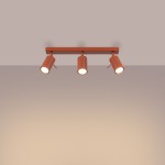 Lampa sufitowa Ring w kolorze ochra czerwona z trzema reflektorami GU10, zamontowana na prostokątnej podstawie. Reflektory mają cylindryczny kształt i są skierowane w dół, tworząc równomierne oświetlenie. Tło w jasnym odcieniu.