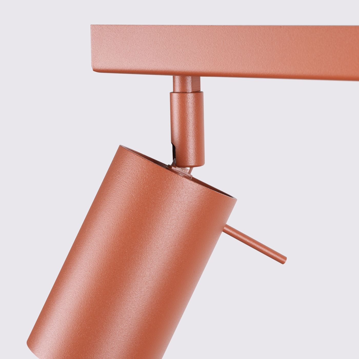 Lampa sufitowa spot w kolorze ochra czerwona z trzema źródłami światła GU10. Ujęcie z boku, pokazujące cylindryczny klosz oraz mechanizm obrotowy. Matowa powierzchnia, minimalistyczny design, zamontowana na prostokątnej podstawie.