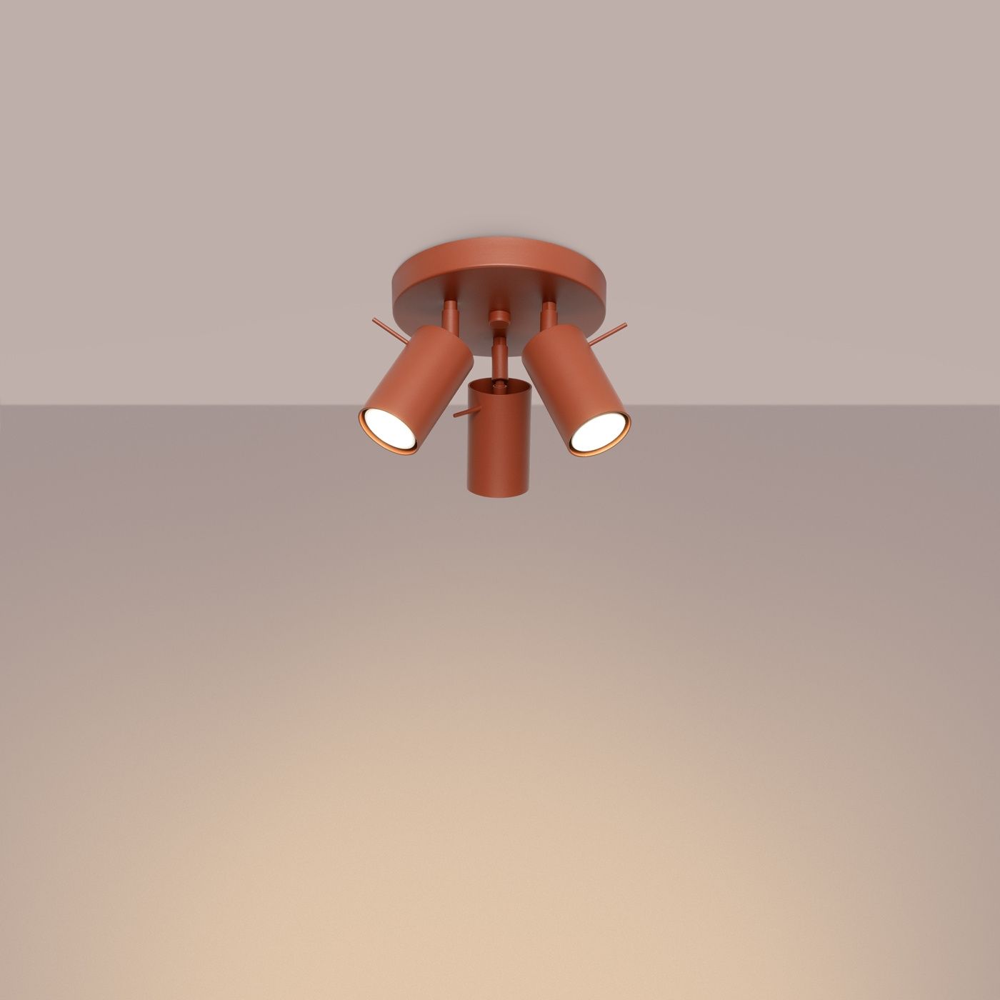 Lampa sufitowa typu spot w kolorze ochra czerwona, z trzema regulowanymi kloszami, zamontowana na okrągłej podstawie. Klosze mają cylindryczny kształt, a ich wnętrza są białe, co zapewnia efektywne oświetlenie.