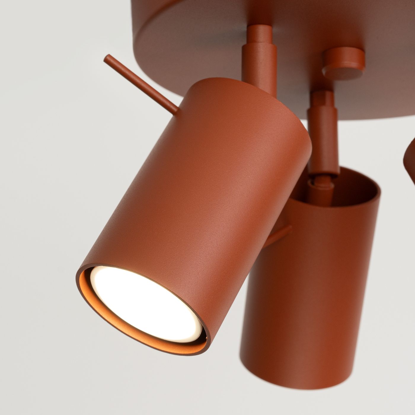 Lampa sufitowa Ring w kolorze ochra czerwona z trzema ruchomymi reflektorami GU10. Metalowa konstrukcja z matowym wykończeniem. Ujęcie z bliska, pokazujące detal jednego z reflektorów oraz mechanizm mocowania.