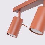 Lampa sufitowa spot w kolorze ochra czerwona, z czterema ruchomymi kloszami GU10. Ujęcie z bliska na dwa klosze, cylindryczny kształt, matowa powierzchnia, zamontowana na prostokątnej podstawie.