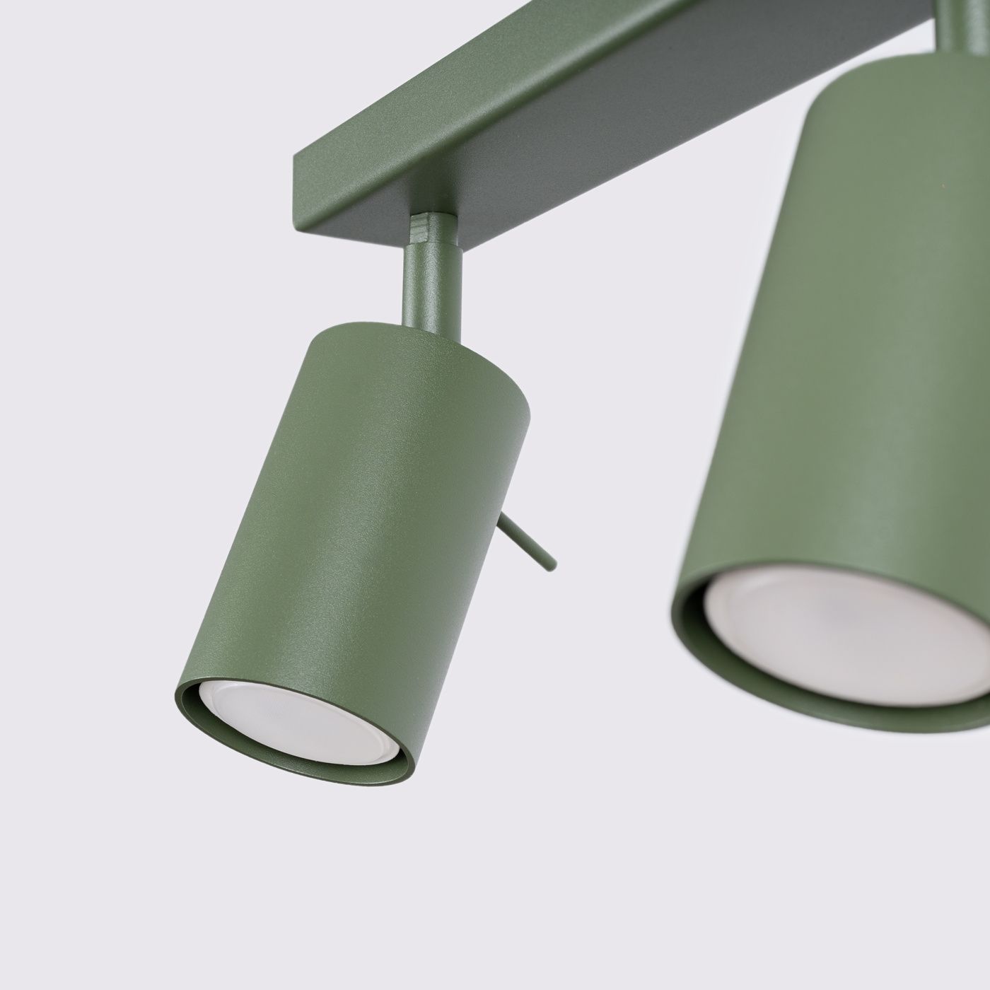 Lampa sufitowa Ring w kolorze oliwkowym, z czterema punktami świetlnymi GU10. Kąt ujęcia: zbliżenie na dwa cylindryczne klosze z matowego metalu, zamontowane na prostokątnej podstawie. Prosta konstrukcja z widocznymi mocowaniami.