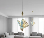 Lampa wisząca Mariposa z pojedynczym źródłem LED 8W, w kolorze złotym. Klosz w kształcie motyla, wykonany z kolorowych, szklanych fragmentów w odcieniach niebieskiego, złotego i brązowego. Zawieszona na cienkim kablu w nowoczesnym wnętrzu.