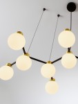 Lampa wisząca Caminos z czarnym metalowym stelażem i złotymi detalami, posiada sześć okrągłych kloszy z mlecznego szkła, zawieszona na cienkich linkach. Montaż sufitowy, nowoczesny design.