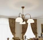 Żyrandol Opal 3xE27 w patynie, z trzema kloszami w kształcie półkul, zawieszony na estetycznych łukach. W tle widoczne eleganckie zasłony i meble, tworzące przytulną aranżację wnętrza.