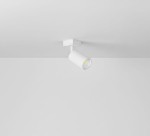 Biała lampa sufitowa typu spot, zamontowana na suficie, cylindryczny kształt z metalowym elementem w środku. Ujęcie z góry, na jednolitym tle. Idealna do oświetlenia wnętrz w minimalistycznym stylu.