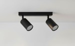 Czarna lampa sufitowa (spot) 2-punktowa z metalowymi kloszami, zamontowana na prostokątnej podstawie. Klosze są cylindryczne, skierowane w różnych kierunkach, co umożliwia regulację oświetlenia. Tło jasne, jednolite.