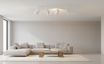 Biała lampa sufitowa (spot) 4-punktowa z okrągłymi kloszami, zamontowana na prostokątnej podstawie. Ujęcie z góry w nowoczesnym wnętrzu z jasnymi ścianami i kanapą. Klosze skierowane w różne strony, zapewniające równomierne oświetlenie.