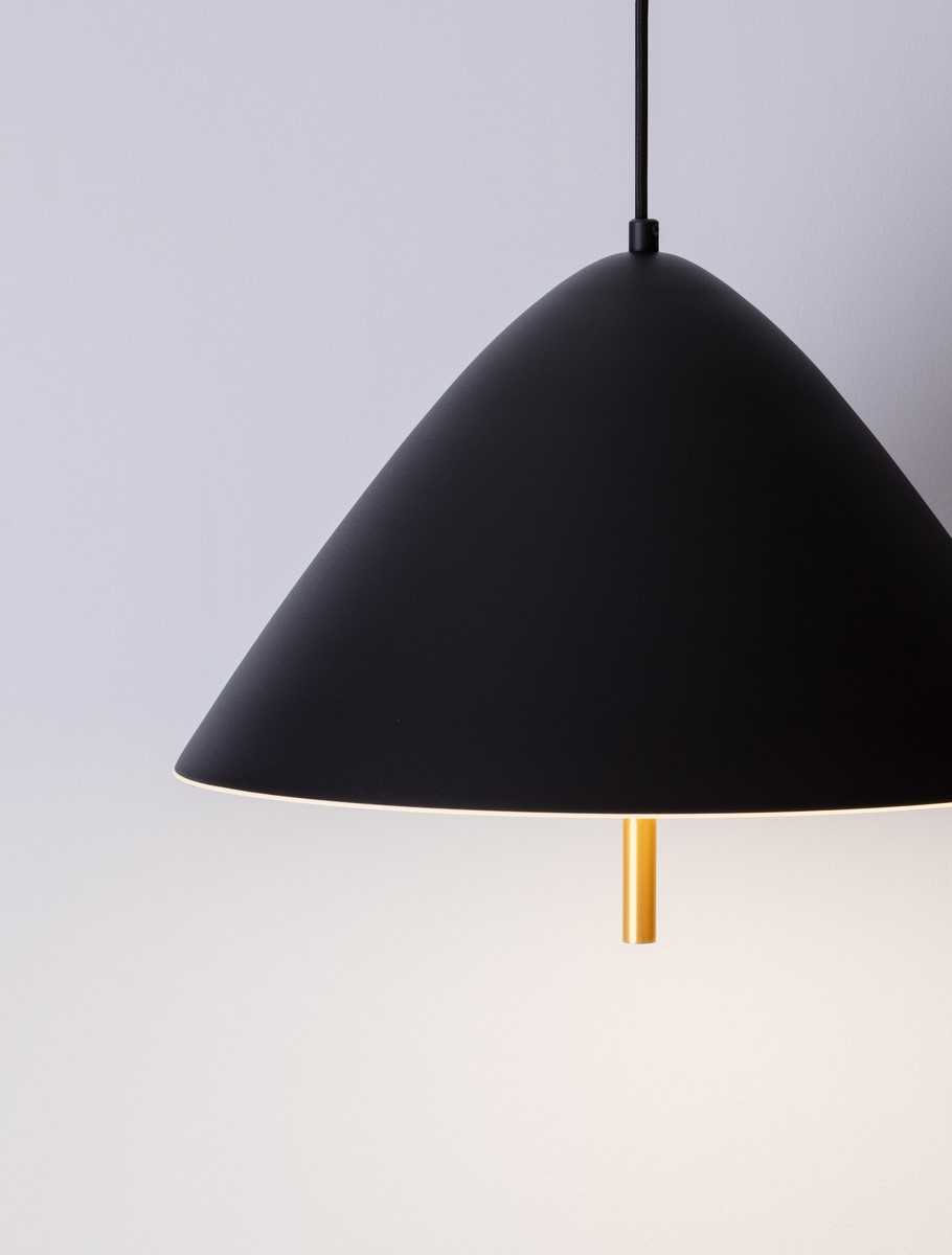 Lampa wisząca Carapari w kolorze czarnym, o kształcie stożkowym, z metalowym elementem w kolorze złotym. Zawieszona na czarnym kablu, zintegrowane źródło światła LED 17W. Tło jasne, co podkreśla elegancki design lampy.