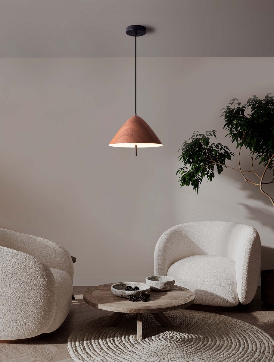 Lampa wisząca Carapari 1xLED 17W w kształcie stożka, wykonana z ciemnego drewna, z czarnym zawieszeniem. Zawieszona na długim kablu, emituje ciepłe światło. W tle minimalistyczne wnętrze z jasnymi fotelami i drewnianym stolikiem.