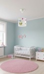 Lampa wisząca Butterfly 1-punktowa, z białym abażurem zdobionym kolorowymi motylkami w odcieniach zieleni, różu i błękitu. Zawieszona na cienkim przewodzie, umieszczona w jasnym pokoju dziecięcym obok łóżeczka i dywanu w kształcie okręgu.