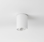 Biała lampa sufitowa w formie tuby, zamontowana na suficie. Okrągły kształt z widocznym mechanizmem kierunkowym wewnątrz. Prosty design, pasujący do nowoczesnych wnętrz. Tło zdjęcia jasne, co podkreśla kolor lampy.