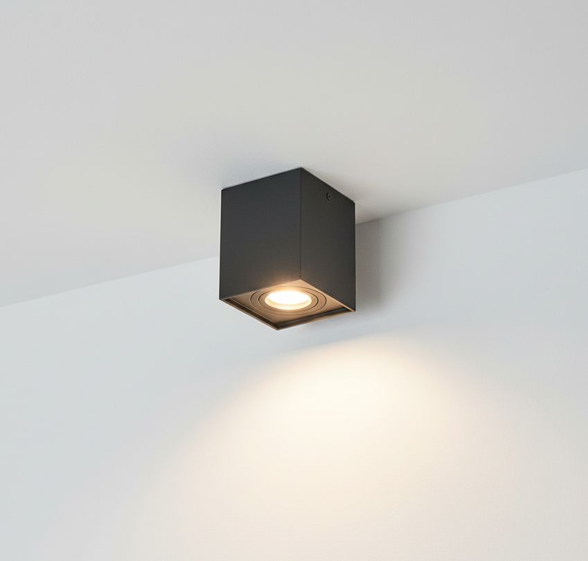 Lampa sufitowa Hadar w kolorze czarnym, w kształcie sześcianu, zamontowana na suficie. Wyposażona w jedno źródło światła GU10, skierowane w dół, na białym tle. Prosta, nowoczesna forma idealna do oświetlenia wnętrz.
