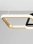 Lampa wisząca Chulumani 2xLED 36W w kolorze czarnym z elementami złotymi. Posiada nowoczesny, geometryczny kształt z wyraźnymi liniami. Zawieszona na cienkiej, przezroczystej linki, idealna do aranżacji wnętrz. Tło w odcieniu szarym.