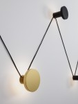 Kinkiet Cliza z pięcioma źródłami LED, o mocy 34W, w kolorze czarnym i złotym. Wyposażony w okrągłe, matowe elementy zamocowane na czarnych kablach, zamontowany na białej ścianie, z subtelnym podświetleniem.