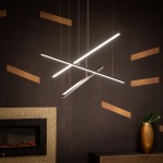 Czarna lampa wisząca Trio LED ściemnialna, 3-punktowa, z trzema prostokątnymi, poziomymi elementami świetlnymi, zawieszona na cienkich linkach. Tło w ciemnym drewnie z dekoracyjnymi złotymi pasami oraz nowoczesnym kominkiem w aranżacji wnętrza.
