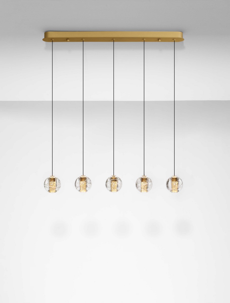Lampa wisząca Cuyo z pięcioma źródłami LED 16W, złota konstrukcja z metalowym stelażem, szklane klosze w formie kul z widocznymi elementami. Zawieszona na cienkich linkach, montowana do sufitu, z minimalistycznym tłem.