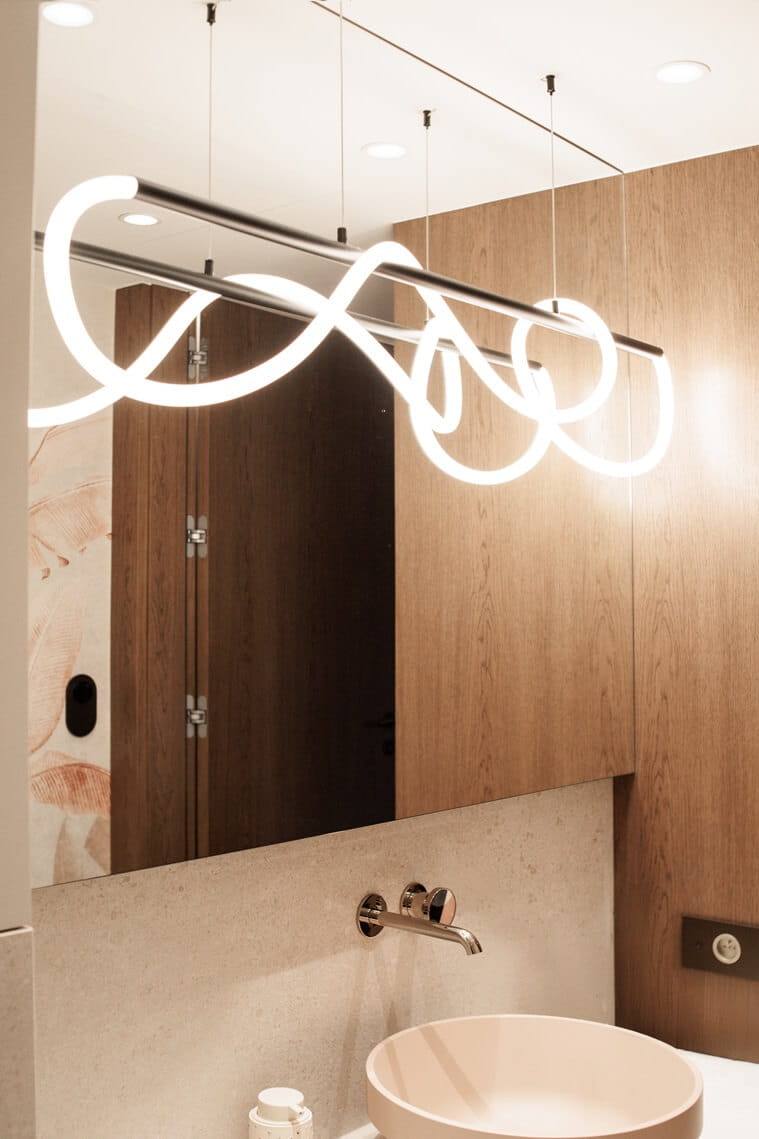 Lampa wisząca Laguna w kolorze czarnym, z jedną żarówką LED o mocy 30W. W kształcie falistych linii, zawieszona na cienkich linkach, z metalowym stelażem. Widoczna w nowoczesnej łazience z drewnianymi elementami i jasnym tłem.