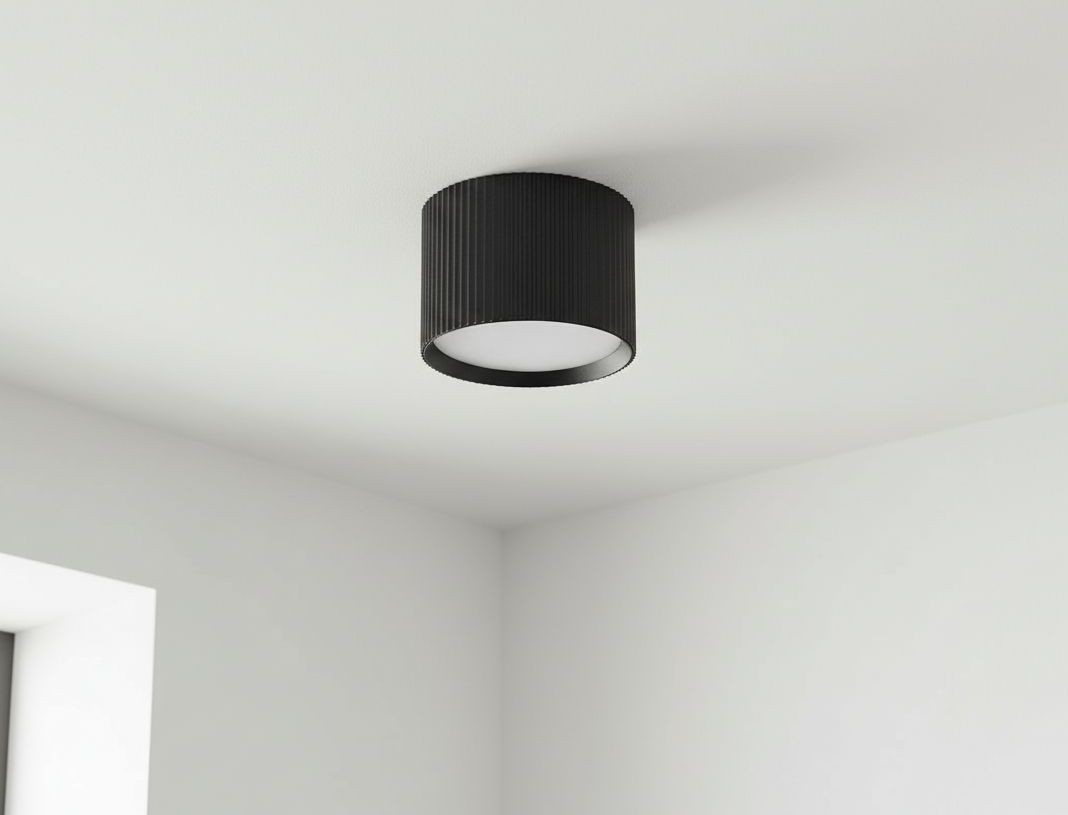 Czarna lampa sufitowa Gisele w kształcie tuby z żarówką GX53, zamontowana na białym suficie. Lampa ma teksturowaną, cylindryczną obudowę i okrągłą, białą osłonę, emitującą światło w dół.