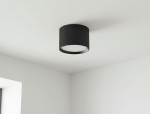Czarna lampa sufitowa Gisele w kształcie tuby z żarówką GX53, zamontowana na białym suficie. Lampa ma teksturowaną, cylindryczną obudowę i okrągłą, białą osłonę, emitującą światło w dół.