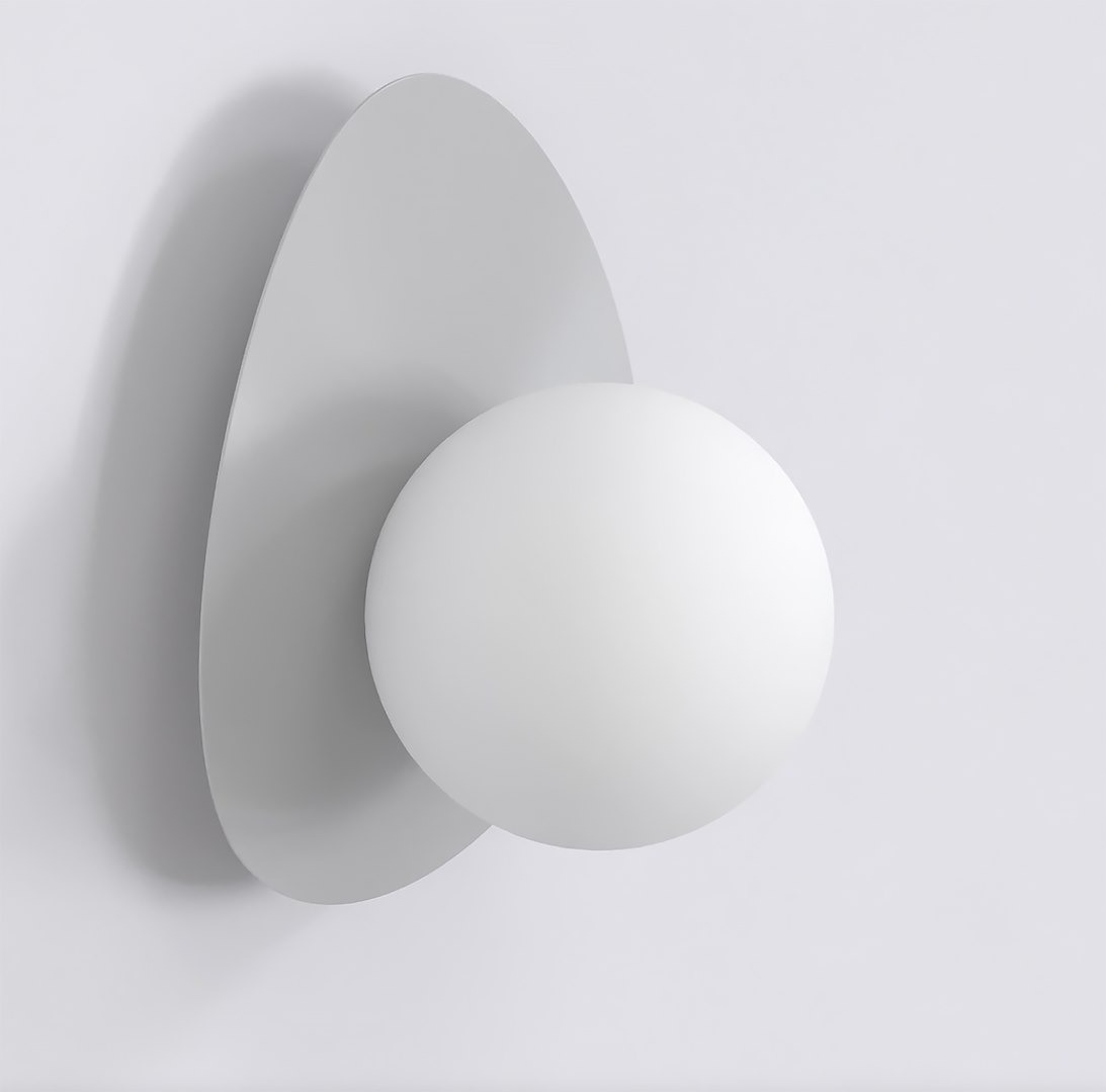 Kinkiet Ovo w kolorze szarym, z jedną oprawą G9. Posiada zaokrąglony, matowy klosz w białym kolorze, umieszczony na owalnej, szarej podstawie. Zawieszony na jasnym tle, ukazany z przodu.