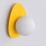 Kinkiet Ovo 1xG9 w kolorze pomarańczowym z okrągłą białą oprawą na tle gładkiej, jasnej ściany. Lampa ma zaokrąglony, żółty element montażowy w kształcie owalnym. Produkt zamontowany na ścianie, widoczny z przodu.