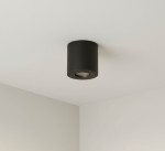 Czarna lampa sufitowa w kształcie tuby, montowana na suficie. Wykonana z materiałów odpornych na wilgoć (IP54). Widok z dołu, ukazujący okrągłą oprawę oraz źródło światła w środku. Tło jasne, minimalistyczne.