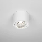 Biała lampa sufitowa tuba kierunkowa Arcos, zamontowana na suficie. Okrągła obudowa z metalicznym wykończeniem, z widoczną żarówką w szklanym kloszu. Kąt ujęcia z góry, podkreślający minimalistyczny design.